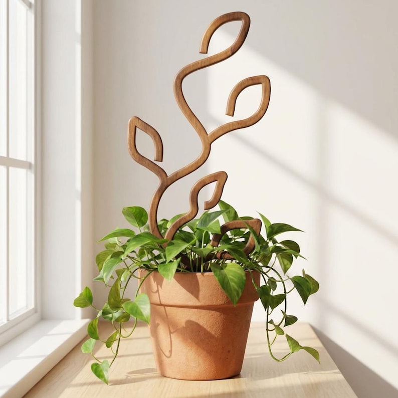 May include: A brown wooden plant trellis with a curved, vine-like structure featuring leaf-shaped cutouts. The trellis is inserted into a terracotta-colored pot containing a green leafy plant with trailing stems and heart-shaped foliage.