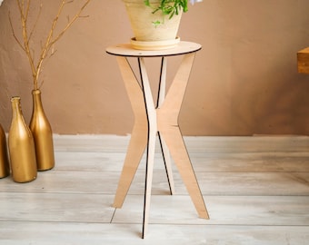 May include: A light wood plant stand with a round top and three legs. The stand is made of plywood and has a natural finish.