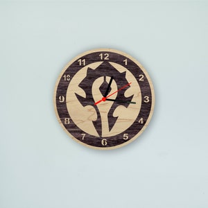 Könnte beinhalten: Eine Holzuhr mit einem schwarz-weißen Design des Horde-Symbols aus World of Warcraft. Das Zifferblatt der Uhr hat schwarze Zahlen und einen roten Stundenzeiger und einen schwarzen Minutenzeiger.