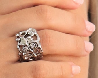 May include: A silver ring with a unique, organic design featuring multiple small clear stones.