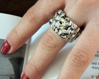 May include: A silver ring with a textured, organic design. The ring is worn on a finger with red nail polish.