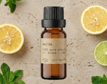以下が含まれることがあります： 黒いキャップと「mojito 100% pure essential oil blend | 15ml aire candle」と書かれたベージュのラベルが付いた小さな琥珀色のガラス瓶。新鮮な緑のミントの葉、丸ごとの黄色いレモン、スライスされた黄色いレモンと緑のライムに囲まれています。