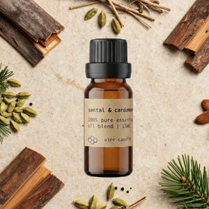 Santal & Cardamom 100% pure essential oil blend by Aire Candle Co. in a 15 ml amber glass bottle, styled with smooth sandalwood pieces, green cardamom pods, cedarwood bark, vetiver and fresh pine sprigs. This warm, woodsy-spiced blend combines creamy sandalwood depth with subtle aromatic spice—perfect for creating a cozy, grounding, and sophisticated home ambiance.