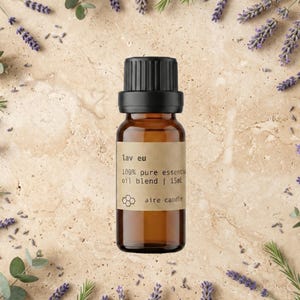 May include: A small amber glass bottle with a black cap and a tan label. The label features the text "lav eu", "100% pure essential oil blend | 15ml", and a honeycomb icon above the text "aire candle". The bottle is surrounded by lavender.