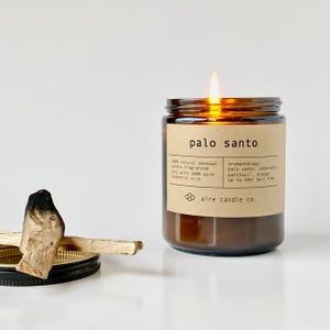 Palo Santo scented beeswax candle. Next to the candle is a black metal lid with Palo Santo sticks on top of them.