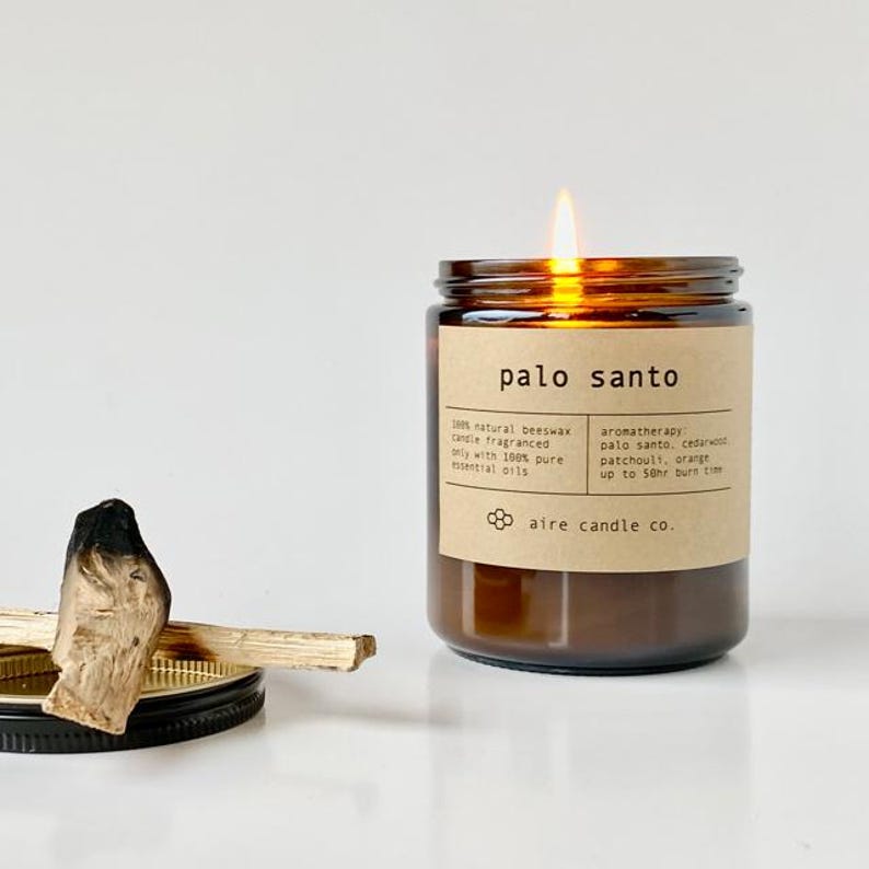 Palo Santo scented beeswax candle. Next to the candle is a black metal lid with Palo Santo sticks on top of them.