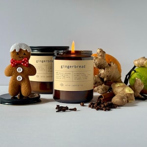 Gingerbread scented beeswax candles. In the foreground is the 8 oz candle with a flame. The background contains scent notes like ginger, clove, nutmeg, vanilla, cinnamon, orange and bergamot.