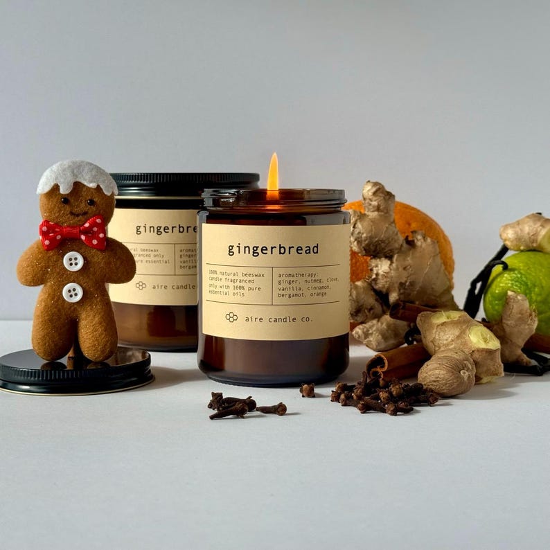 Gingerbread scented beeswax candles. In the foreground is the 8 oz candle with a flame. The background contains scent notes like ginger, clove, nutmeg, vanilla, cinnamon, orange and bergamot.