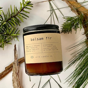 Balsam Fir beeswax candle laying flat with coniferous scent notes surrounding it (fir needles, cedarwood, cypress and pine needles).