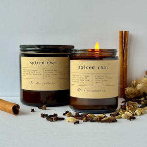 Spiced Chai scented beeswax candles. The 16 oz jar to the left and the 8 oz jar to the right. In the background are scent cues such as a cinnamon sick, cardamom seeds, ginger, vanilla beans and clove.