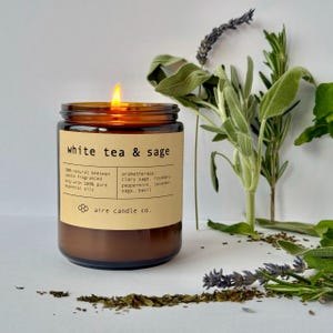 White Tea & Sage candle lit with scent notes behind it. The scent notes are Sage, Lavender, Basil, Rosemary and Peppermint.