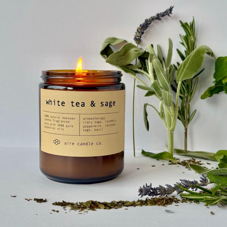 White Tea & Sage candle lit with scent notes behind it. The scent notes are Sage, Lavender, Basil, Rosemary and Peppermint.