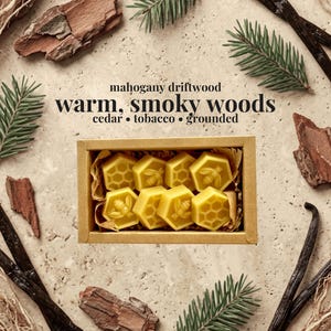 May include: A rectangular cardboard box containing eight yellow wax melts in hexagonal shapes, featuring bee and honeycomb patterns. The text reads: mahogany driftwood, warm, smoky woods, cedar, tobacco, grounded. The box is surrounded by pine needles.