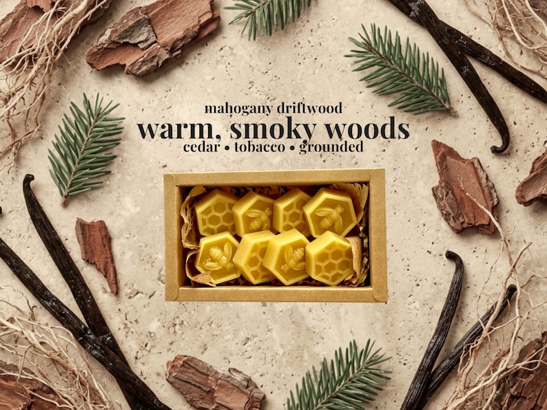 May include: A rectangular cardboard box containing eight yellow wax melts in hexagonal shapes, featuring bee and honeycomb patterns. The text reads: mahogany driftwood, warm, smoky woods, cedar, tobacco, grounded. The box is surrounded by pine needles.