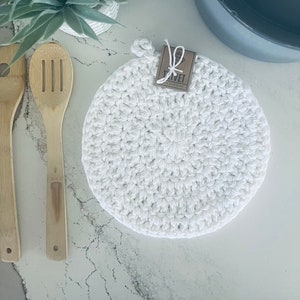 Puede incluir: Posavasos de ganchillo blanco con una etiqueta marrón que dice "Trivet" sobre una superficie de mármol blanco.