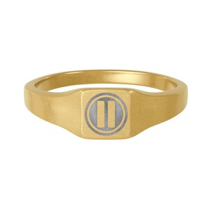 May include: A gold signet ring with a square face. The face has a grey circle with two vertical lines. The ring has a brushed metal finish and a rounded band.