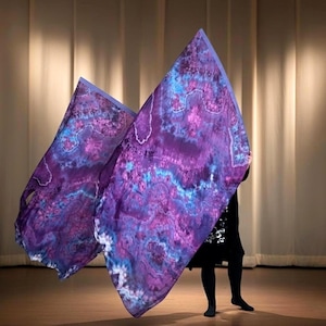 May include: Two flowing, tie-dye fabric flags in shades of purple, blue, and white. The flags are held by a person, creating a dynamic display. The fabric has a marbled effect, with a light blue border.