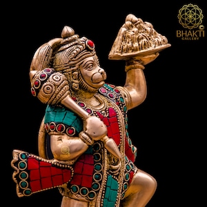 K&ouml;nnte beinhalten: Eine goldfarbene Statue der hinduistischen Gottheit Hanuman, die in der einen Hand eine Keule und in der anderen eine Schale mit Opfergaben h&auml;lt. Die Statue ist mit roten und gr&uuml;nen Edelsteinen verziert.