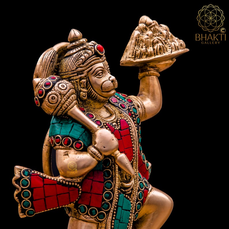 K&ouml;nnte beinhalten: Eine goldfarbene Statue der hinduistischen Gottheit Hanuman, die in der einen Hand eine Keule und in der anderen eine Schale mit Opfergaben h&auml;lt. Die Statue ist mit roten und gr&uuml;nen Edelsteinen verziert.