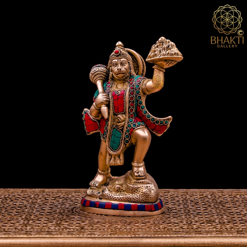 K&ouml;nnte beinhalten: Eine goldfarbene Statue der hinduistischen Gottheit Hanuman, die in der einen Hand einen Berg und in der anderen einen Kn&uuml;ppel h&auml;lt. Die Statue ist mit roten und t&uuml;rkisfarbenen Edelsteinen verziert.