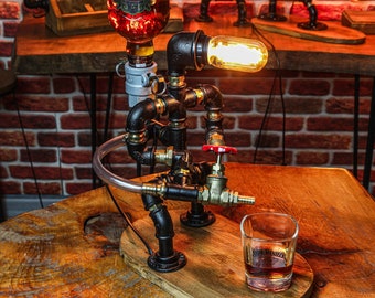 May include: A steampunk-style liquor dispenser made from black pipes and fittings, with a clear glass bottle, a red valve, and a clear glass shot glass. The dispenser has a light bulb with a warm glow.