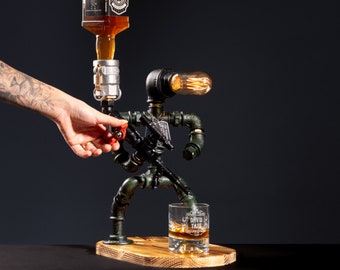 May include: A green metal liquor dispenser shaped like a robot with a light bulb for a head. The dispenser is pouring liquor into a glass with the text "David Tate" on it.