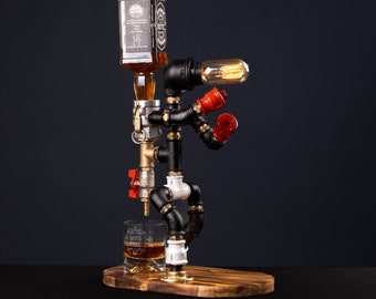 Peut inclure: Un distributeur de liqueur en métal noir et blanc en forme de personne avec un interrupteur lumineux rouge et un verre transparent avec une inscription personnalisée. Le distributeur tient une bouteille de whisky et la verse dans le verre.