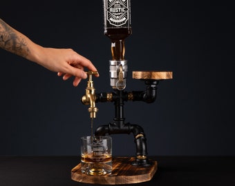 May include: A black metal liquor dispenser with a gold faucet, a wooden base, and a glass of whiskey. The dispenser is shaped like a person with a bottle of whiskey on top. The bottle has a label that says "RUSTIC" on it.