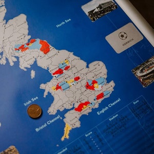 Peut inclure: Une carte du Royaume-Uni avec des points color&eacute;s marquant des emplacements. La carte est sur un fond bleu avec les noms des mers et des canaux &eacute;tiquet&eacute;s. Il y a une pi&egrave;ce de monnaie sur la carte pr&egrave;s de l'&eacute;tiquette "Mer d'Irlande".