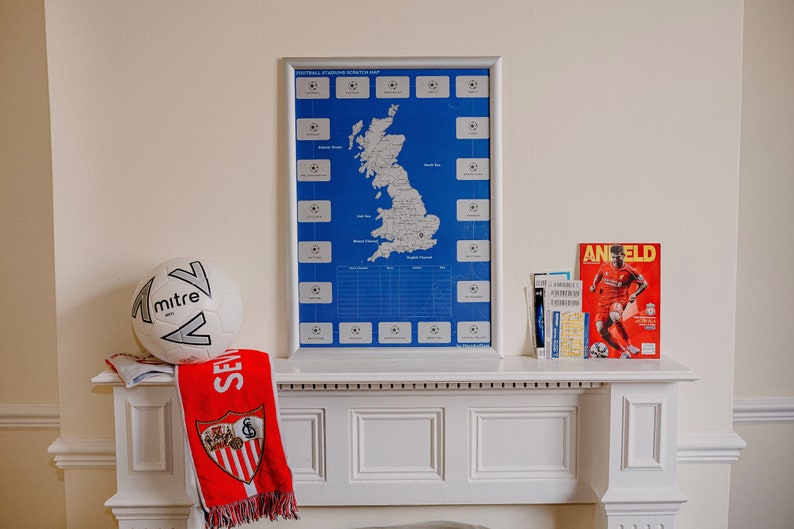 Peut inclure: Un ballon de football blanc avec un logo "mitre" noir et argent&eacute; est pos&eacute; sur une chemin&eacute;e blanche. Une &eacute;charpe de football rouge et blanche avec un blason est drap&eacute; sur la chemin&eacute;e. Une carte encadr&eacute;e du Royaume-Uni avec les stades de football marqu&eacute;s est accroch&eacute;e au mur au-dessus de la chemin&eacute;e. Une pile de billets et un magazine avec le mot "Anfield" sur la couverture sont sur le c&ocirc;t&eacute; droit de la chemin&eacute;e.