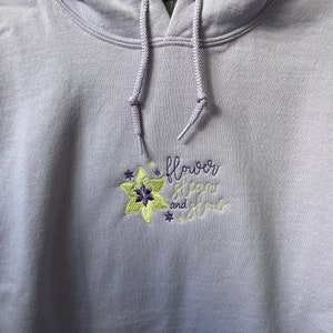 Może przedstawiać: Bordowa bluza z kapturem z haftowanym wzorem kwiatu i tekstem "flower stem and flow".