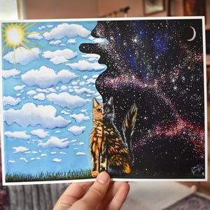 May include: A watercolor painting depicting a cat split down the middle, with one side representing daytime and the other nighttime. The daytime side shows a blue sky with clouds and a sun, while the nighttime side features a starry galaxy and a crescent moon.