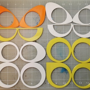May include: A set of 12 craft shapes in various sizes and colors. The shapes are made of a thick, durable material and are perfect for crafting projects. The shapes include circles, ovals, and half-circles. The colors are orange, yellow, and white.