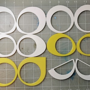 May include: A set of white and yellow craft shapes, including circles, ovals, and semi-circles. The shapes are cut from foam board and are arranged on a grid.