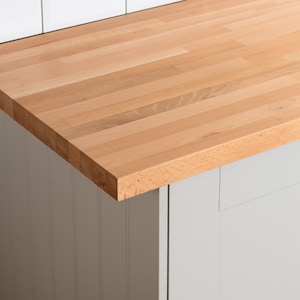 May include: A close-up of a light wood worktop with a smooth, slightly textured surface. The worktop is made of multiple planks of wood, creating a natural wood grain pattern.
