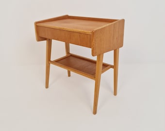 May include: A light wood end table with a drawer and a shelf. The table has a simple, mid-century modern design.