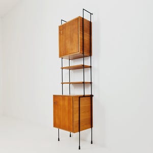 May include: A vintage wall-mounted shelving unit with a mid-century modern design. It features two wooden cabinets with a light brown finish, supported by black metal rods and shelves. The unit is designed for storage and display.