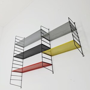 May include: A set of four black metal wall shelves with a grid pattern. The shelves are in different colors: red, yellow, black, and gray.