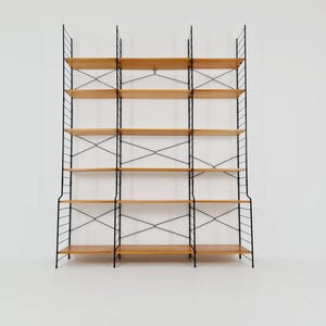 Op de afbeelding: Een hoge, modulaire boekenplank met meerdere houten planken ondersteund door een zwart metalen frame. De planken zijn lichtbruin van kleur en het frame heeft een minimalistisch ontwerp. De unit is vrijstaand.