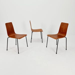 Puede incluir: Tres sillas de madera con patas de metal negro. Las sillas están dispuestas en forma triangular sobre un fondo blanco.