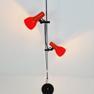 Puede incluir: Una l&aacute;mpara de pie de cromo con dos pantallas ajustables rojas. La l&aacute;mpara tiene una base negra y un cable largo.