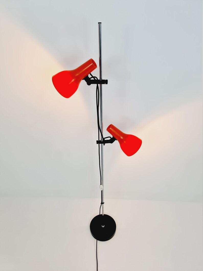 Puede incluir: Una l&aacute;mpara de pie de cromo con dos pantallas ajustables rojas. La l&aacute;mpara tiene una base negra y un cable largo.