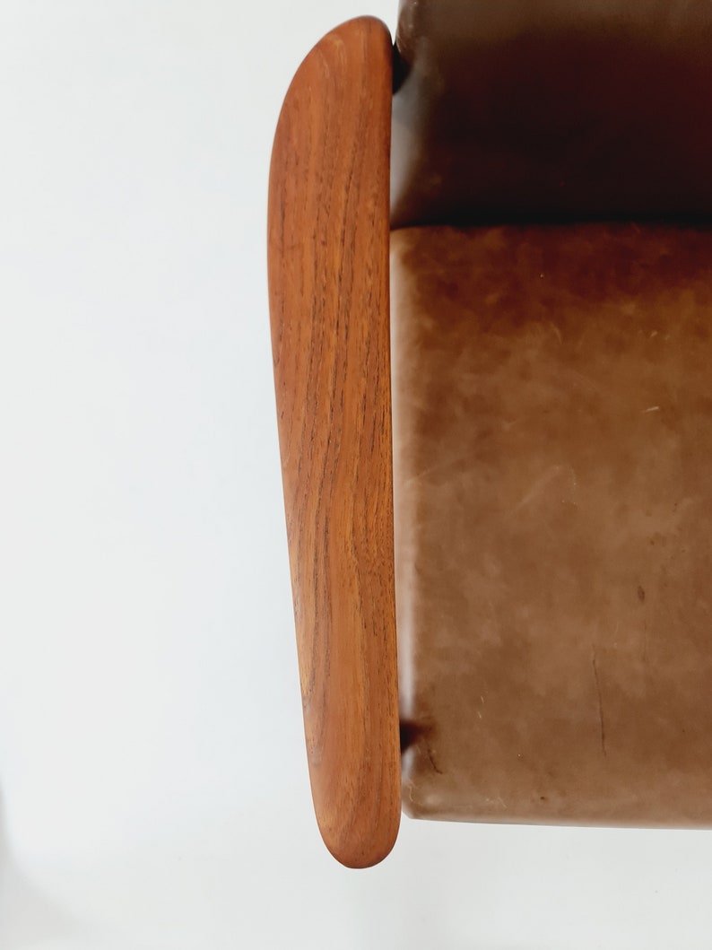 May include: Close-up of a brown leather chair with a wooden armrest. The armrest is curved and has a natural wood grain.