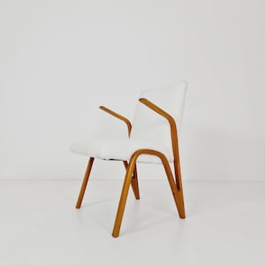 Può includere: Una poltrona imbottita bianca con gambe e braccioli in legno. La poltrona ha un design semplice e moderno.