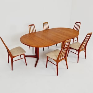 Puede incluir: Un juego de comedor de madera compuesto por una mesa ovalada con base central de pedestal y seis sillas. Cada silla presenta un respaldo alto con listones verticales y un asiento tapizado en tela de color beige claro. La madera es marrón.