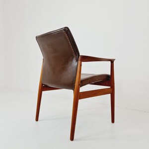 May include: A brown leather armchair with a wooden frame. The chair has a high back and a low seat. The chair is shown from the back, with the back legs visible.