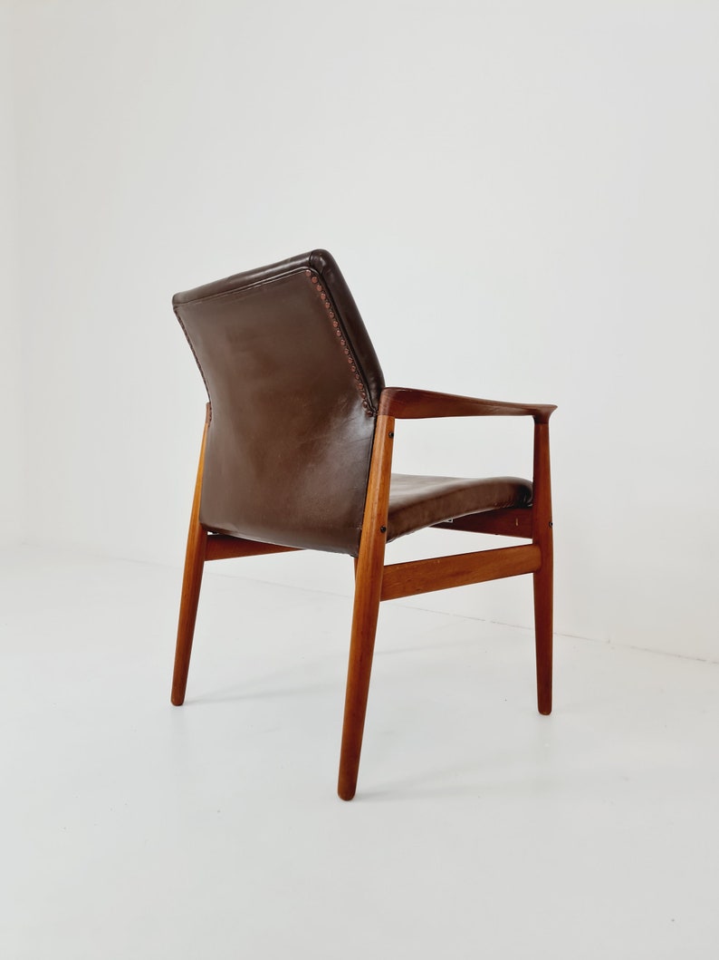 May include: A brown leather armchair with a wooden frame. The chair has a high back and a low seat. The chair is shown from the back, with the back legs visible.