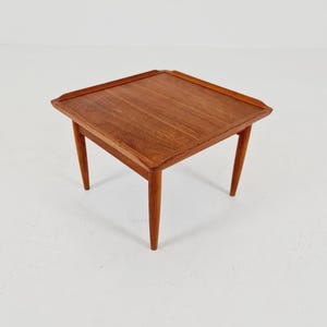 Peut inclure: Une table d'appoint carrée en bois avec une finition brun chaud, dotée d'une surface supérieure plate aux bords légèrement surélevés et de quatre pieds fuselés qui s'étendent vers l'extérieur depuis les coins, offrant une base stable.