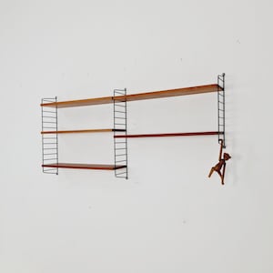 May include: A black metal wall shelf unit with three wooden shelves. The shelves are made of a light brown wood. A wooden monkey figurine is hanging from the bottom shelf.