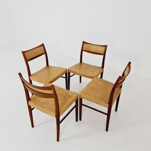 May include: Four mid-century modern dining chairs with a light brown leather upholstery and dark wood frames.
